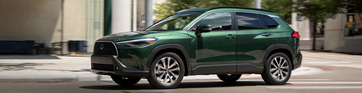 A deep green 2025 Corolla Cross drives through a city