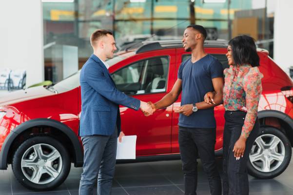 A young couple shakes hands with a salesman to seal the deal on a red SUV