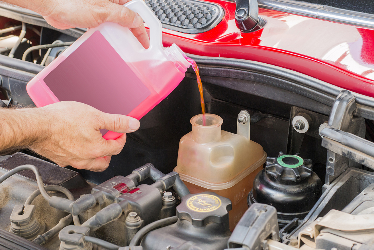 a pair of hands pours pink liquid into a car's reservoir