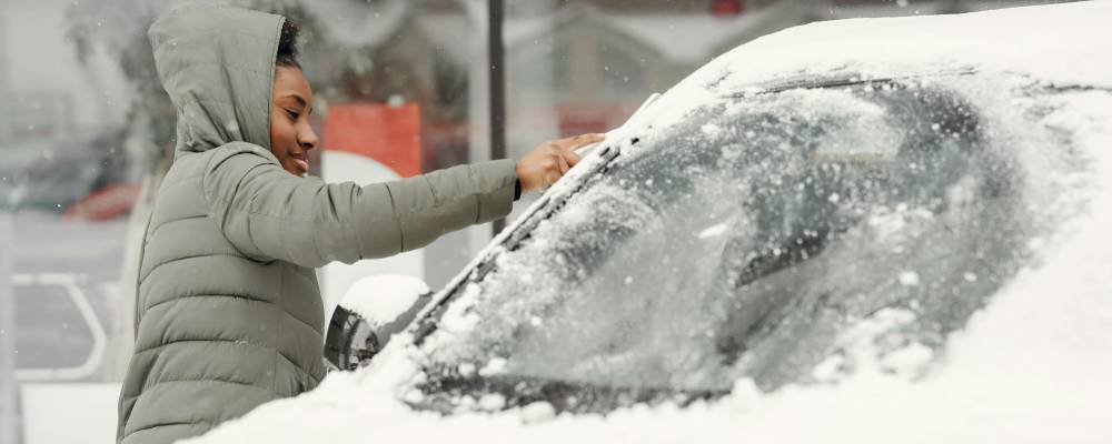 A person in a winter jacket cleans snow off their car windshield