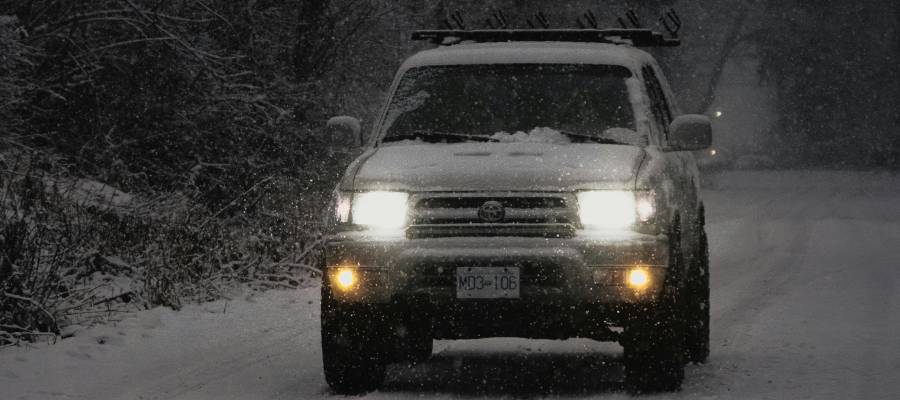 An SUV drives through snow with its headlights on. Headlight service and winter driving tips at Heffner Toyota in Kitchener, ON